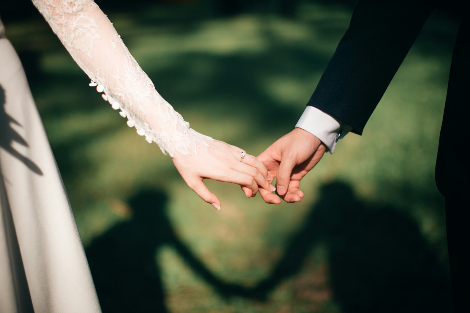 Bride and groom holding hands on sunlit lawn