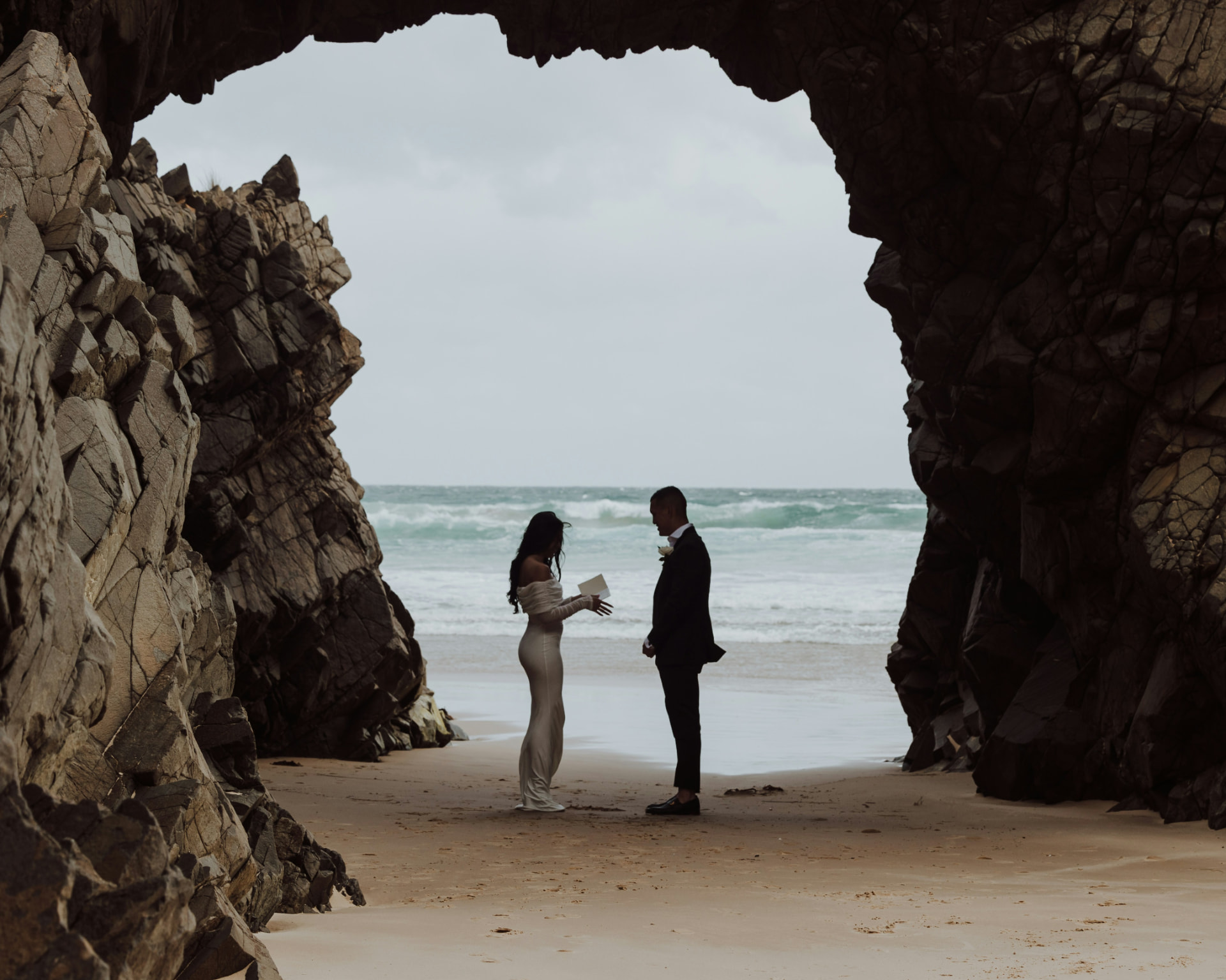 Couple exchanging vows on a beach framed by a rock arch